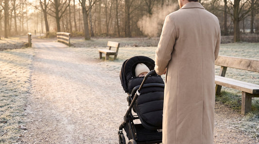 Ouder wandelt met een buggy met zwarte voetenzak van Laavir door een winters park